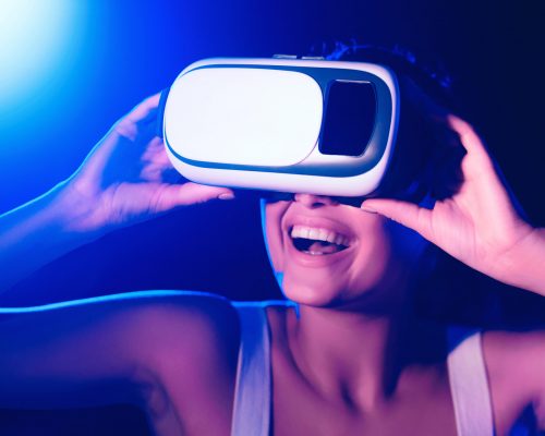 Girl using VR goggles in colorful neon lights, having fun in studio